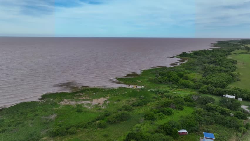 A drone shot gliding over the Río de la Plata estuary, capturing the expansive waterway, surrounding coastline, and natural landscape from an aerial perspective.