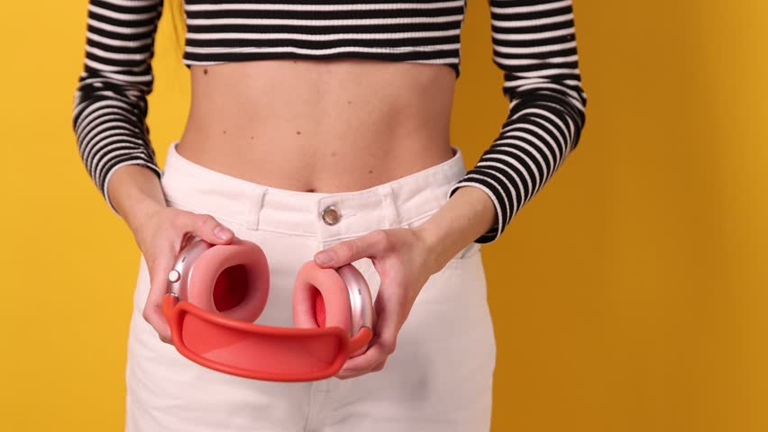 Woman with headphones listening to music and dancing on yellow background
