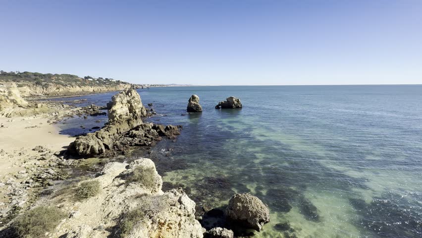 a gorgeous summer landscape at the beach with large rocks in silky brown sand surrounded by blue ocean water and waves rolling into the beach with powerful clouds at sunset at Leadbetter Beach 