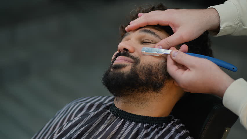 Professional barber shaping beard with straight razor