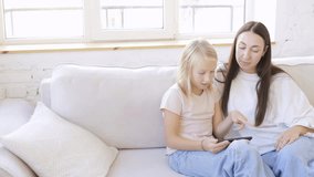 Daughter showing smartphone screen to her mother while sitting together on sofa at home. Family moment of digital learning and entertainment, sharing knowledge through technology - Powered by Shutterstock - Get 15% off with code: PIKWIZARD15