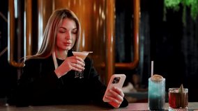 Young woman at nightclub bar holding a cocktail while checking her smartphone, relaxed and enjoying nightlife ambiance and social connection - Powered by Shutterstock - Get 15% off with code: PIKWIZARD15