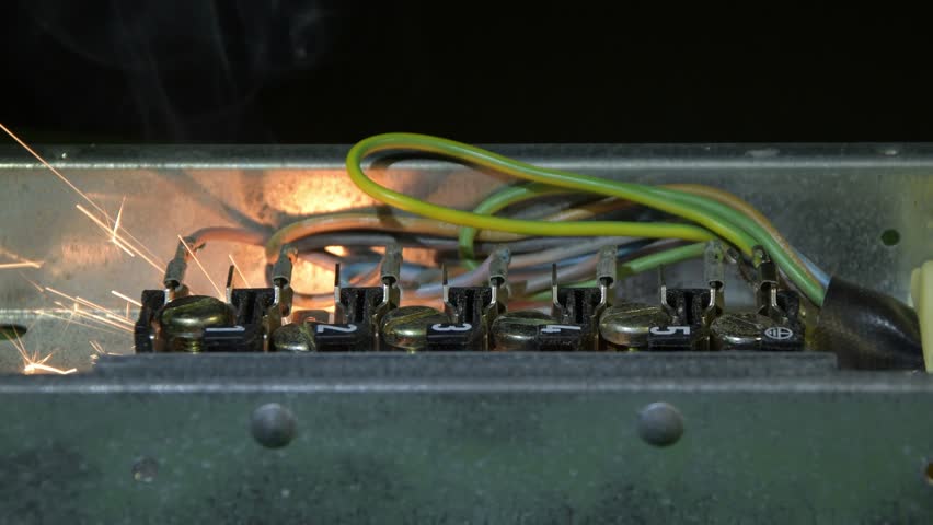 An open electrical panel demonstrates a short circuit with intense sparks and smoke.