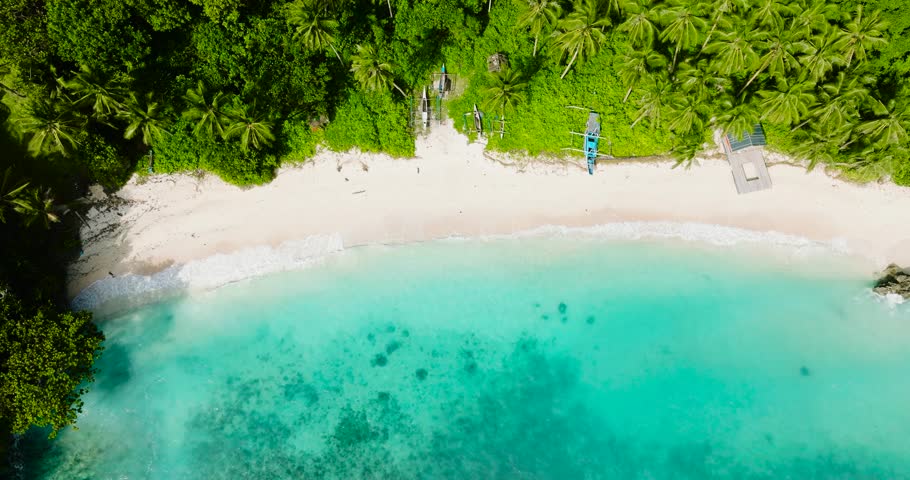 Beach landscape with sun reflection over boats over the sand and turquoise sea waves. Carabao Island, Romblon. Philippines.