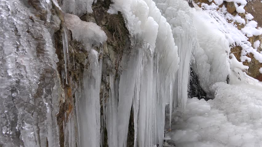 Many crowded icicles cover a natural frozen waterfall in cold air during winter. Winter conditions create dense ice formations as water freezes into clustered shapes.