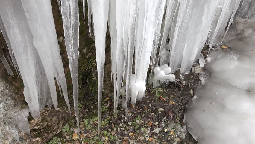 Many crowded icicles cover a natural frozen waterfall in cold air during winter. Winter conditions create dense ice formations as water freezes into clustered shapes.