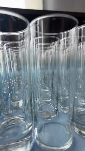 A row of tall, clear glass cups are lined up on a table