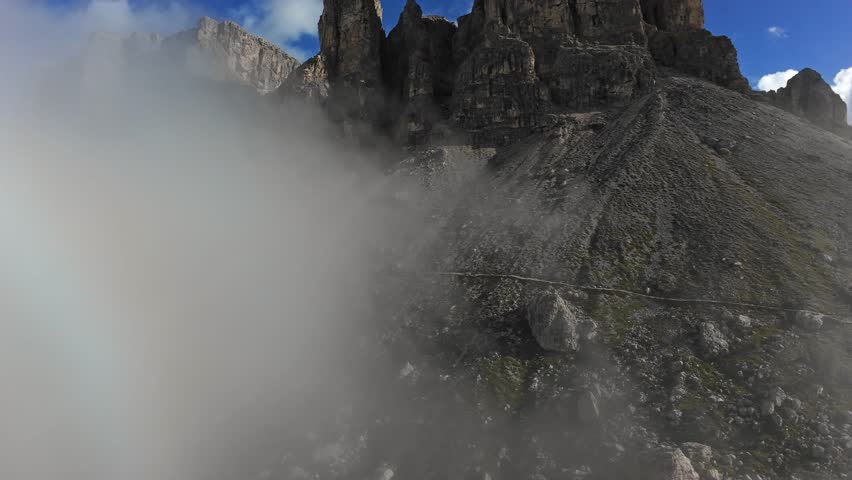 fog rolling across dolomites rocky ridge, low cloud bank sweeping over stone slopes and jagged crags; aerial drone approach, climber traverse scene, via ferrata ascent moment, geologist sampling