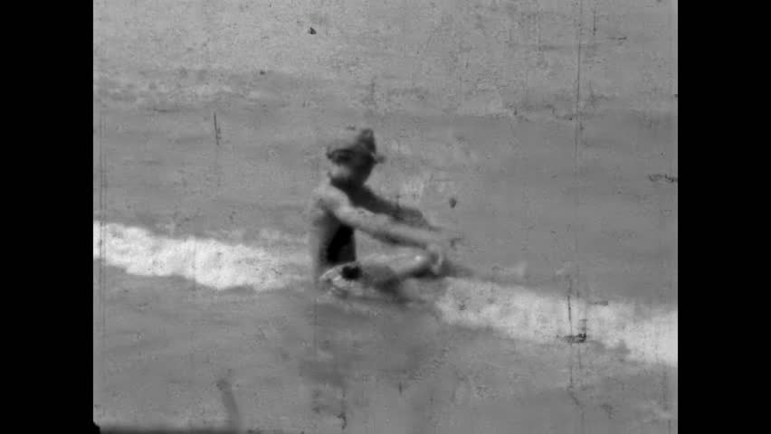 Happy young woman runs into sea to swim. Black and white film. Carefree summer vacation. Female in bikini adjusting cap, playing along shoreline. Old film. Archival retro 1960s. Vintage archive.
