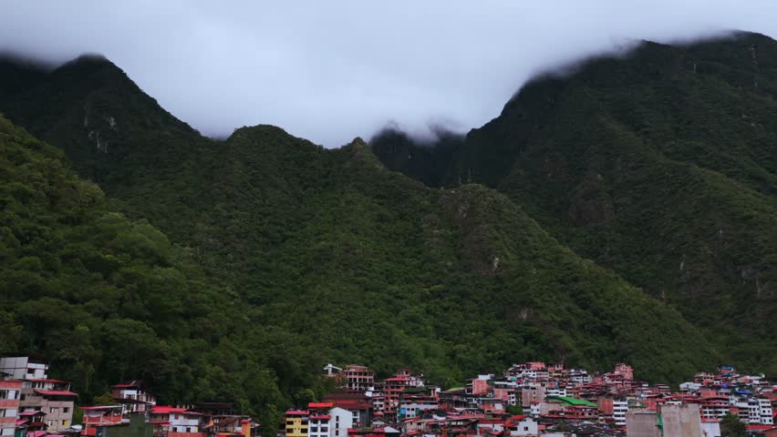 Aguas Calientes Machu Picchu town rainy season cloudy afternoon Peru aerial drone Peruvian Andes Mountains Urabumba river jungle lower highlands Inca trail citadel landscape buildings pan left