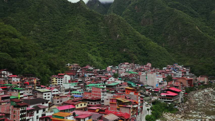 Aguas Calientes Machu Picchu town rainy season cloudy afternoon Peru aerial drone Peruvian Andes Mountains Urabumba river jungle lower highlands Inca trail citadel landscape buildings forward pan up