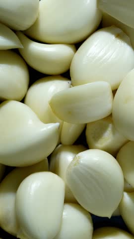 Rotating pile of peeled garlic cloves in top view. 4k vertical concept