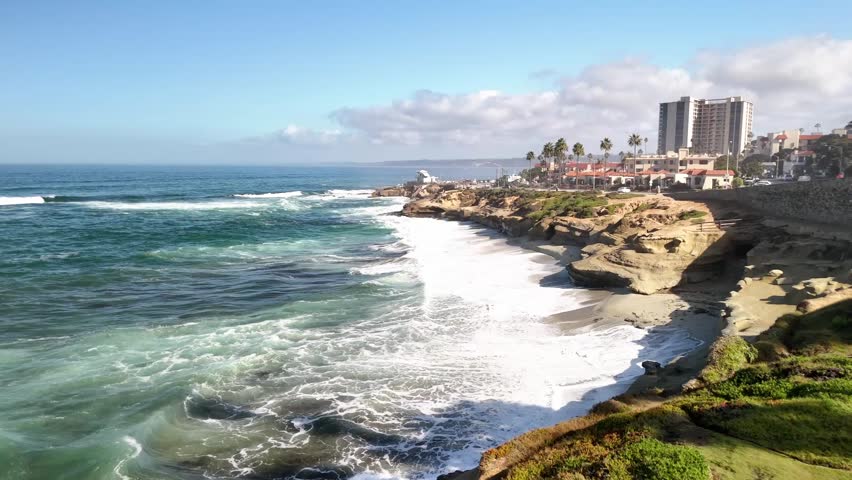 A clean midday drone view featuring rugged rocks and shimmering blue Pacific Ocean water in La Jolla near Torrey Pines and San Diego Ca.