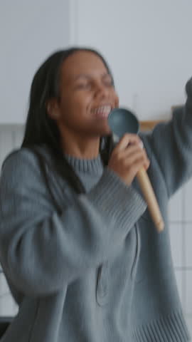 Joyful black woman dancing and singing at home, positive emotions in weekend. African american lady singing favorite song and listening to music in kitchen when cooking dinner or breakfast, have fun