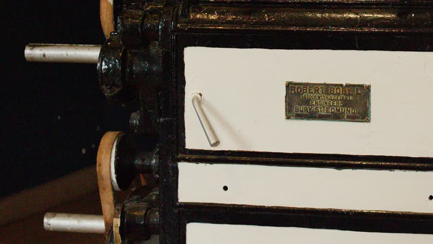 Camera slowly pans vintage gearbox machinery in historic distillery, warm indoor lighting, close-up view