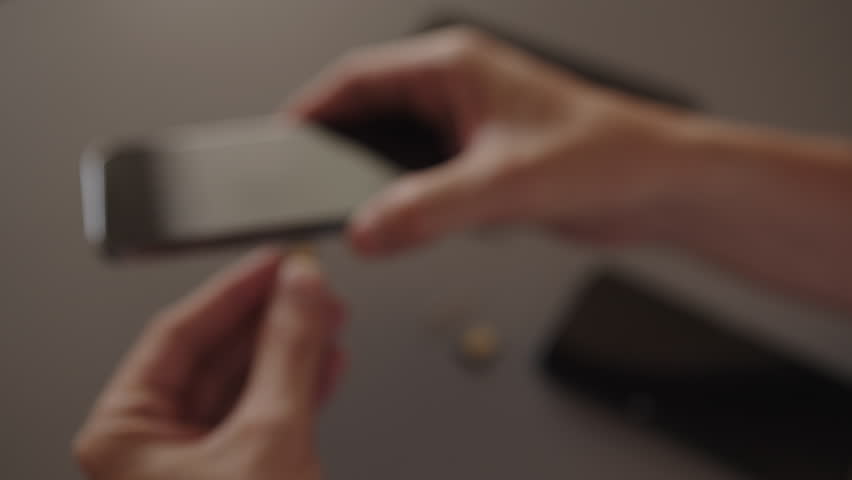 Close-up top view of person holding and inserting nano sim card into new smartphone tray sitting on desk, illustrating mobile service transfer, setup, and device upgrade connectivity, slow motion.