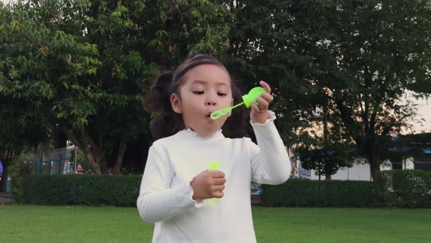 slow motion of happy toddler girl blowing soap bubbles in the park