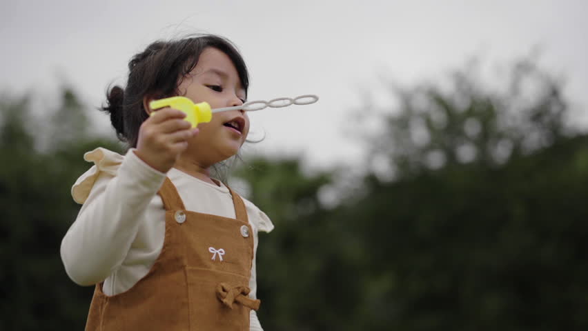 slow motion of happy toddler girl blowing soap bubbles in grass field