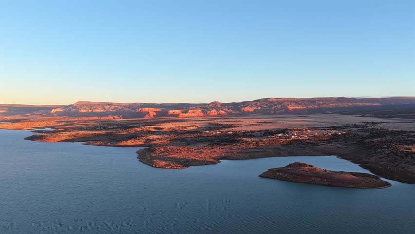 Drone footage moves smoothly along the dramatic red rock cliffs and clear blue water of Abiquiu Lake, New Mexico. This striking high desert landscape is evocative of the Southwest mesas.