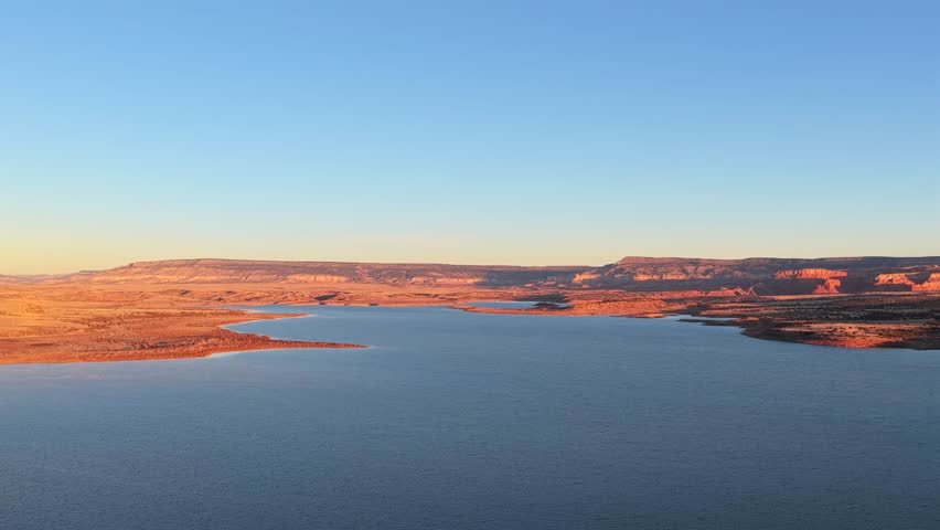 Breathtaking aerial footage captures the sunrise over Abiquiu Lake, New Mexico, bathing the rugged red rock and high desert landscape in a warm, golden light. Perfect Southwest morning scenery.