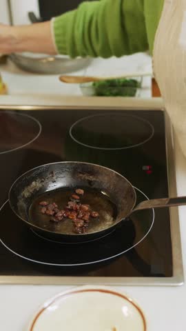 Professional culinary expert pouring golden olive oil into sizzling pan, carefully stirring raisins while preparing gourmet recipe in sleek modern kitchen workspace