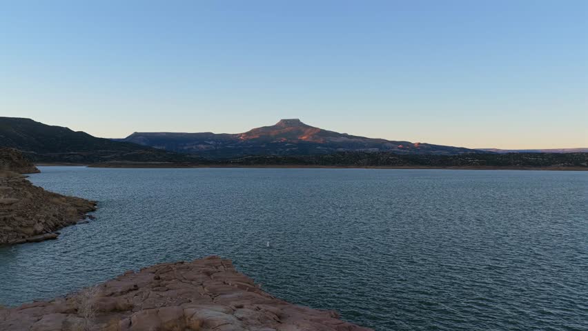 Dramatic drone launch from Abiquiu Lake harbor, ascending to reveal the iconic Cerro Pedernal, a stunning New Mexico mesa made famous by artist Georgia O