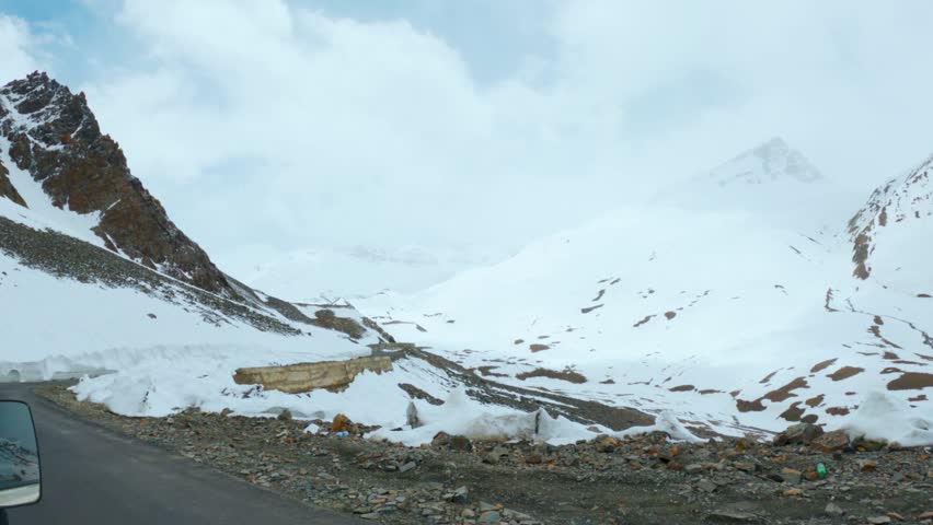 4K shot of thick layer of snow on side of mountain road during winter season at Lahaul, Himachal Pradesh, India. Slippery and risky condition of highway roads during winter. Winter background. 