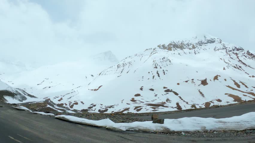 Mountain road under heavy snow, tranquil winter scene as seen from Baralacha pass, Himachal Pradesh, India.  Thick layer of snow on both side of road and stormy weather at Leh Manali Highway, Himachal Pradesh, India. Roadtrip travel concept.
