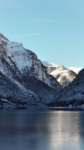 Klöntalersee Switzerland with calm lake, snowy mountains and winter light in peaceful alpine valley, clean vertical mountain landscape.