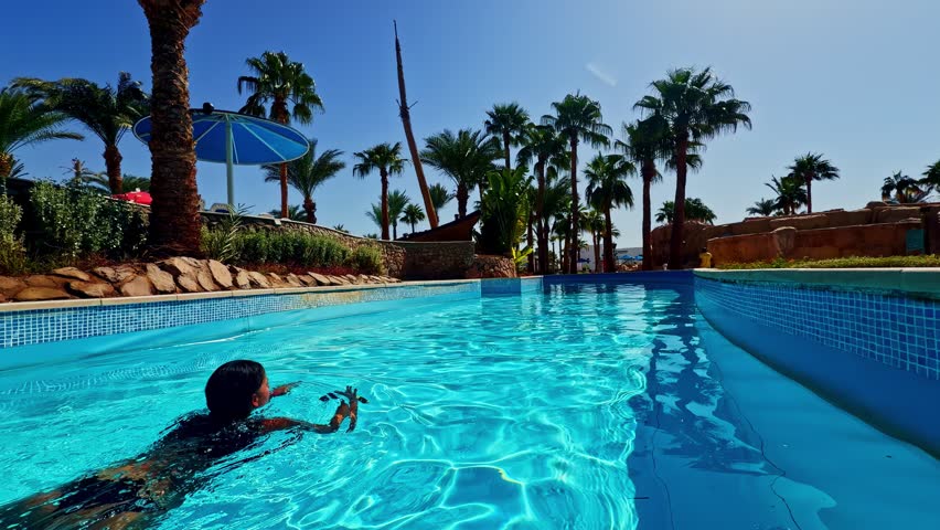Woman enjoys a refreshing swim in crystal-clear infinity pool surrounded by palm trees at a sunny Sharm El-Sheikh resort, Egypt.