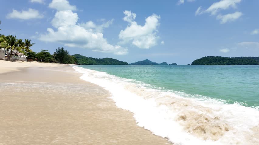 Waves crash on a sandy beach under a blue sky at Tengah Beach. Langkawi Island. Malaysia