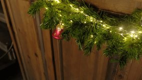 Closeup festive garland, golden bow, warm fairy lights on pine. Shimmering red ornament hanging against wooden wall. Cozy Christmas scene. Warm holiday ambiance. Glowing ornaments. Celebratory decor - Powered by Shutterstock - Get 15% off with code: PIKWIZARD15