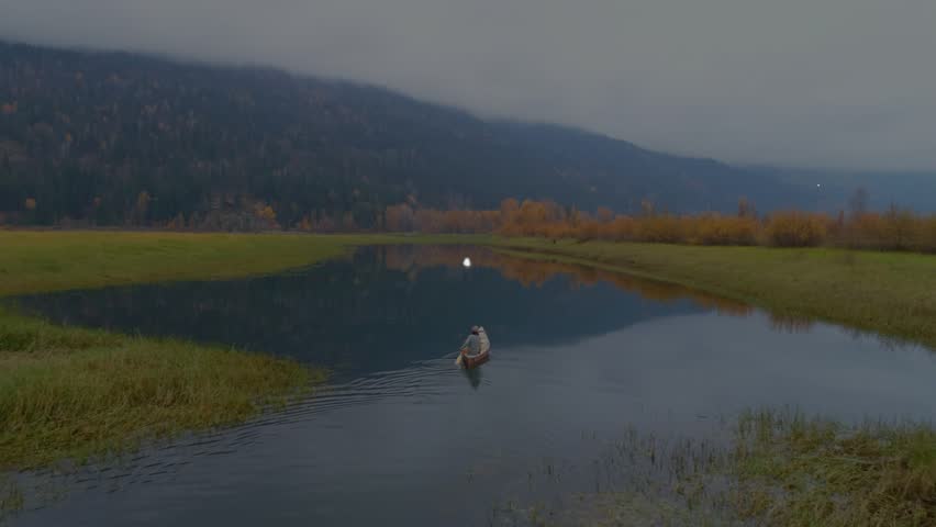 Man paddling rowboat in marsh, HUD overlay appearing around boat and mapping water for tech. Solitude, drone, canoe, wetland, overcast, calm, horizon