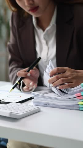 Businesswoman efficiently organizing documents at desk in office. Woman examines, highlights, and organizes documents in an office.