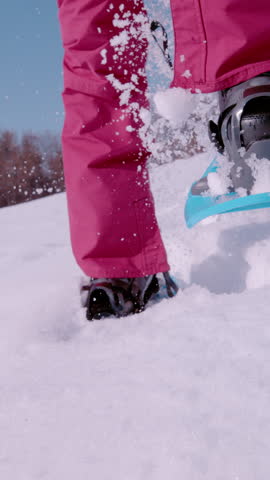 SUPER SLOW MOTION, LOW ANGLE VIEW: Female is running with snowshoes on snowy meadow towards camera. Unrecognizable woman has fun snowshoeing in freshly fallen snow on a beautiful sunny winter day.