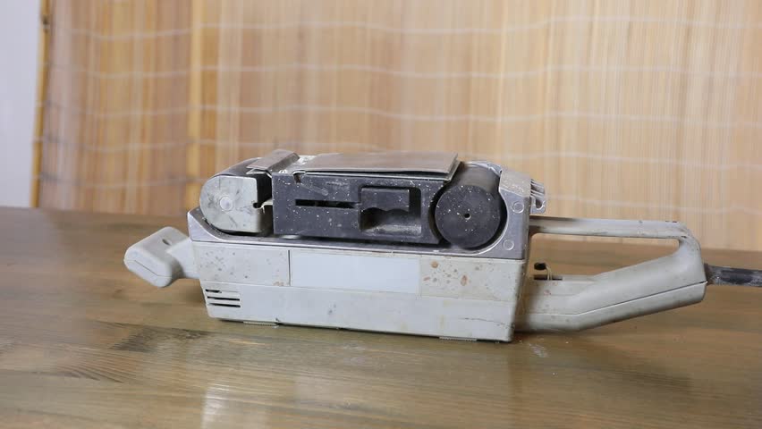 Belt sander sitting on a wooden table, a powerful tool for grinding and sanding various surfaces for woodworking.