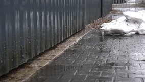 Rainwater flowing along base of grey corrugated metal fence on wet cobblestones near melting snow pile - Powered by Shutterstock - Get 15% off with code: PIKWIZARD15