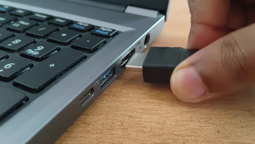Close up of hand plugging or connecting a high definition Multimedia Interface (HDMI) type cable cord in a laptop computer device port hole. Audio or video input and monitor screen share concept.