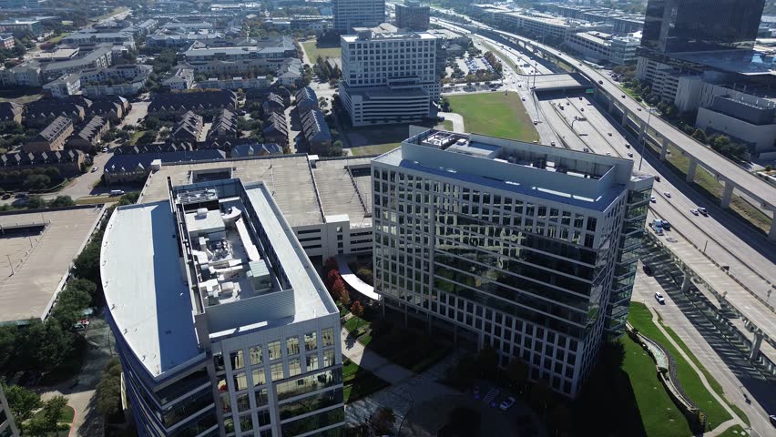 Modern glass office buildings with rooftop HVAC systems border major highway corridor in Plano, Texas, flanked by townhomes, dense parking structures, mixed-use developments suburbs North Dallas. USA