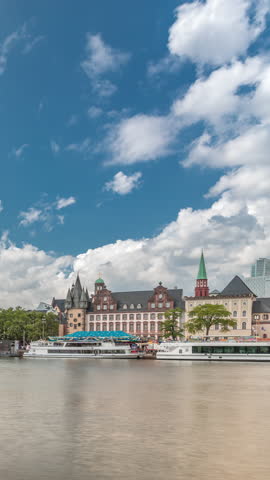 Hyperlapse of the historical Eiserner Steg (Iron Bridge) over the Main River in Frankfurt, Germany. Skyscrapers skyline and historic buildings reflect in the water under a cloud-filled sky timelapse