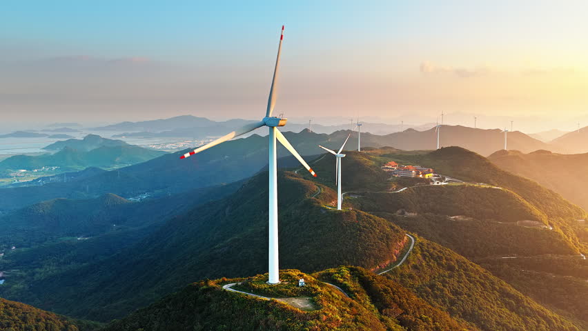 Aerial shot of wind turbines generating clean renewable energy on mountain ridge at sunset