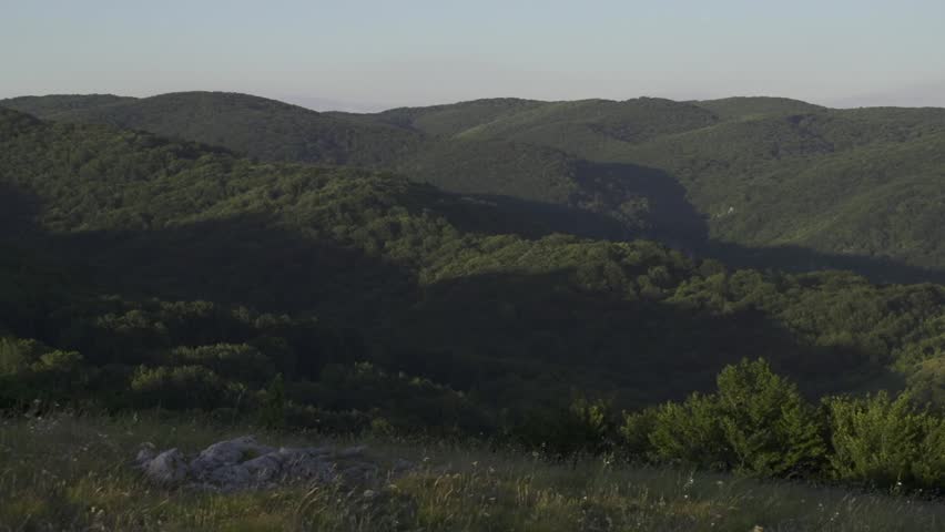 A pan shot of green hills and mountains shows the landscape. Trees cover the mountain. Peak. Kutelka Reserve in Sinite Kamani Nature Park. Stara planina above Sliven town. Balkan Mountains. Bulgaria.
