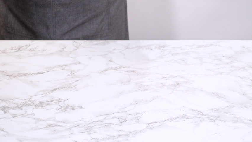 A person places a light blue ceramic baking tray onto a clean marble countertop. The neutral, overhead setup is perfect for kitchen intros, tutorials, or cooking prep scenes.