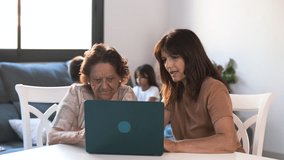 Senior woman learning how to use laptop from daughter in living room while children playing in background at home - Powered by Shutterstock - Get 15% off with code: PIKWIZARD15