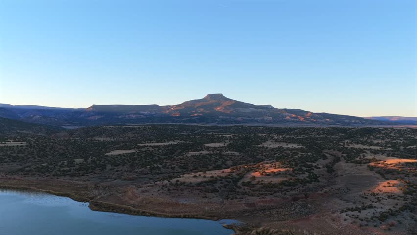 A breathtaking wide panoramic shot of the high desert, showcasing Cerro Pedernal and the still waters of Abiquiu Lake. This New Mexico terrain was made famous by the painter Georgia O'Keeffe.