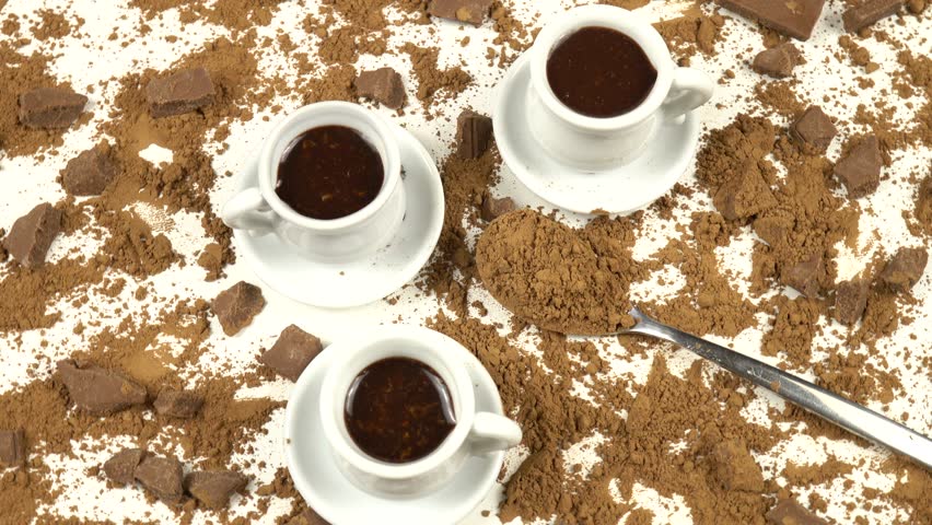 White cups with hot chocolate and a teaspoon with cocoa powder, top view, pieces of milk chocolate on a white background, top view, rotation