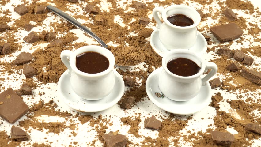 White cups with hot chocolate and a teaspoon with cocoa powder, top view, pieces of milk chocolate on a white background, side view, rotation