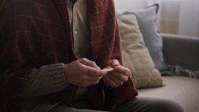 Tilt up shot of ill mature Caucasian man checking temperature with thermometer while sitting on couch wrapped in blanket in living room - Powered by Shutterstock - Get 15% off with code: PIKWIZARD15
