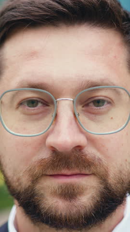 Close-up of a smiling Caucasian man adjusting his glasses and looking at the camera with a blurred background, outdoor