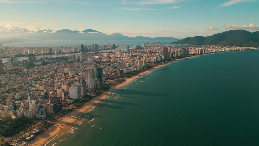 sunny sunset in Vietnamese coastal Da Nang city, My Khe sand beach and touristic My An and Son Tra district with modern skyscraper hotels and resorts, blue sea of Danang, Vietnam, aerial drone view 4k